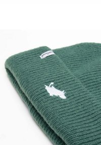 Vihreä neulottu pipo, jossa on ribbineulos, valkoinen eläinlogo ja pieni kangasetiketti reunassa.