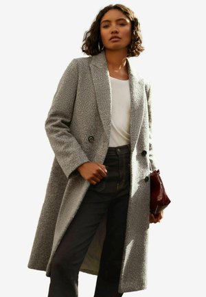 Abrigo de mezcla de lana gris, de doble botonadura, con un acabado texturizado, solapas tipo muesca y botones negros, llevado sobre una blusa blanca y jeans oscuros.