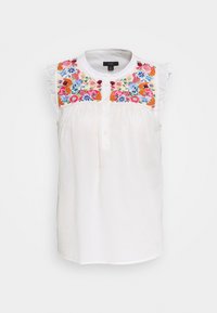 Weiße ärmellose Bluse mit buntem Blumenstickerei auf der Brust und Rüschendetails an den Schultern, ausgestattet mit einem runden Halsausschnitt und einer Knopfleiste.
