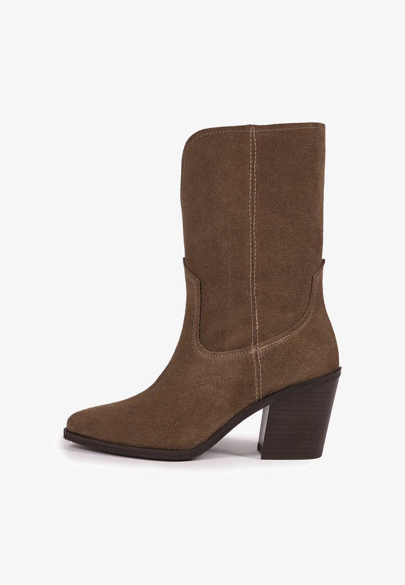 Botte mi-mollet en daim marron avec bout pointu, coutures visibles et talon haut épais empilé sur fond blanc.