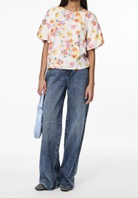 Blommönstrad kortärmad topp i krämfärgad, tillsammans med löst sittande mörk denimjeans. Ljusblå handväska med texturerad yta.