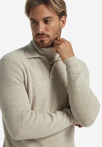Beżowy sweter polo z prążkowanego dzianiny z kołnierzem typu golf, z trzema guzikami i dopasowanymi mankietami, wykonany z miękkiego, teksturowanego materiału.