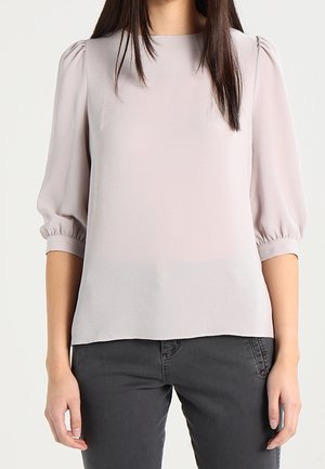 Blusa grigia chiara con maniche a sbuffo e scollatura rotonda. Realizzata in tessuto morbido e testurizzato con una vestibilità rilassata. Abbinata a pantaloni grigi scuri.