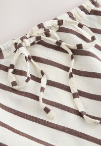 Gros plan d’un tissu crème avec des rayures horizontales marron et une taille à cordon noué.