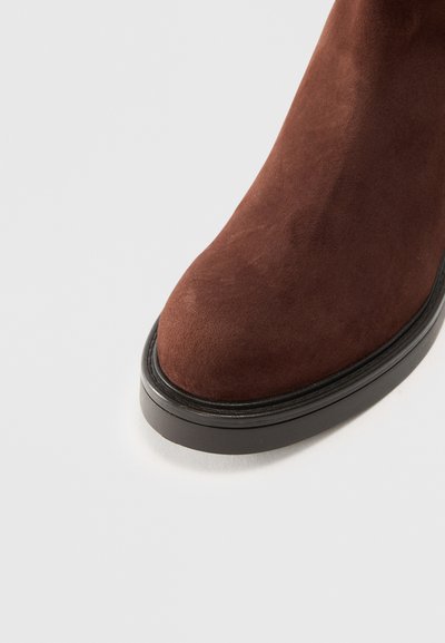 Punta di stivale in suede marrone con suola in gomma nera su sfondo bianco.