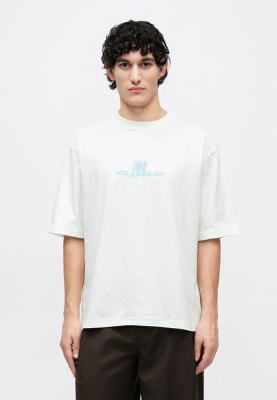 Tricou alb din bumbac cu mâneci scurte, având un logo albastru imprimat în centru cu inscripția "HOLZWIELER WINTERSPORT". Croială simplă, lejeră.