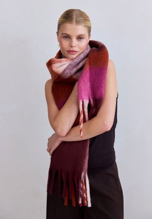 Écharpe en laine chaude et multicolore avec des dégradés de rouge, rose et violet. Présente des extrémités à franges et une finition douce et texturée.