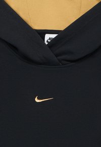 Tumši zili sporta krekli ar kapuci, kas izgatavots no mīksta auduma. Priekšpusē ir zeltīta izšuvuma Nike logo, un tam ir kontrastējoša iekšējā odere.