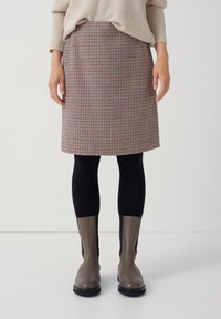Kostkovaná sukně ke kolen v béžové, červené a námořnické modři; strukturovaný design s kapsami, spárovaná s černými legínami a šedými kotníkými botami.