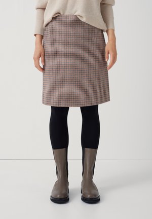 Jupe mi-longue à carreaux beige, rouge et marine ; design structuré avec poches, associée à des leggings noirs et des bottines grises.