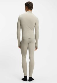 Beżowy termiczny komplet: dopasowany top i spodnie, teksturowana tkanina, długie rękawy z otworami na kciuki oraz legginsy sięgające kostek. Gładkie wykończenie.