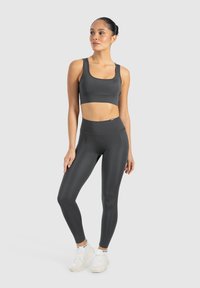 Czarny stanik sportowy i legginsy w ciemnoszarym kolorze, wykonane z elastycznego materiału, charakteryzujące się gładką fakturą i dopasowanym krojem. Białe sneakersy dopełniają całość.