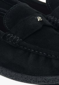 Zwarte suède loafers met gestikte details, een decoratieve strik en een kleine metalen accent. Voorzien van een gestructureerde zwarte rubberen zool.