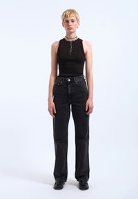 Black ribbed sleeveless top paired with high-waisted straight-leg black jeans. Model wears layered necklaces and black shoes. Simple background.