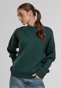 Grüner Sweatshirt mit hohem Kragen, lockerer Passform und gerippten Bündchen und Saum. Der Stoff wirkt weich und strukturiert, kombiniert mit Denim-Jeans.