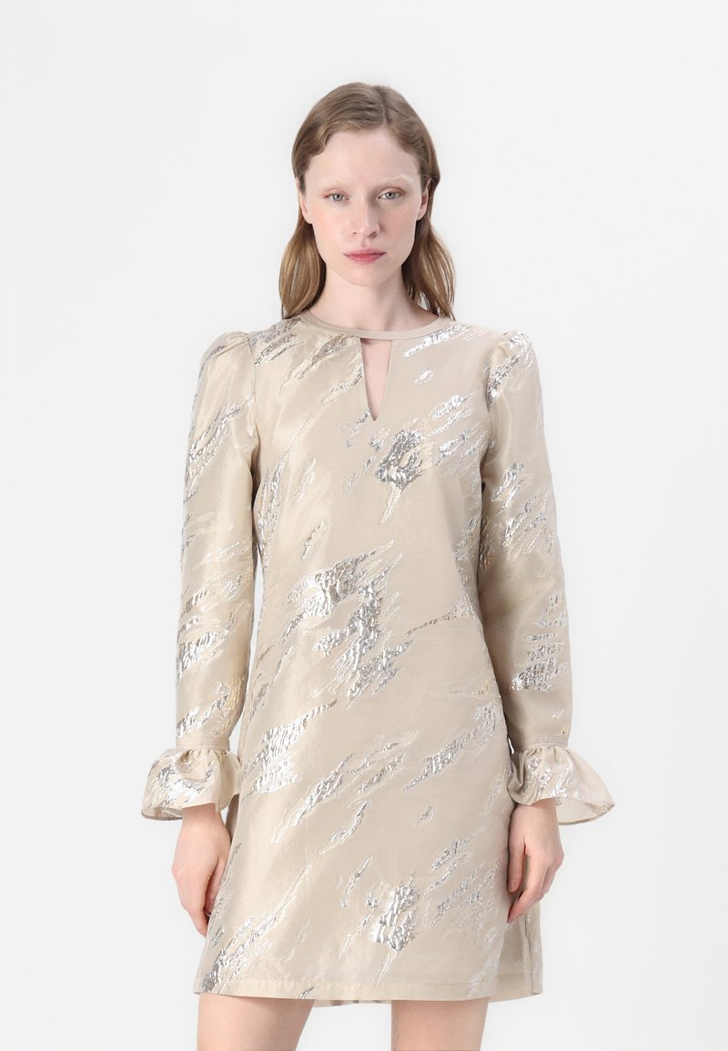 Kreminės spalvos iki kelių siekianti suknelė su metalinių sidabro abstrakčių raštų, ilgos pūkuotos rankovės ir iškirptė raktų angos detale. Slybus audinio paviršius.