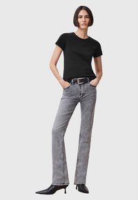 Maglietta nera aderente, jeans dritti grigi chiari a vita alta e tacchi a punta neri. Tessuto liscio con dettagli di cucitura discreti.