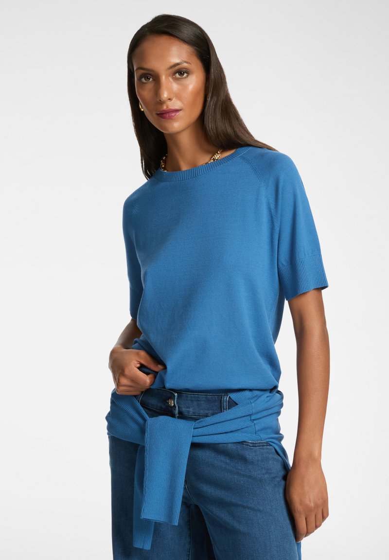 Blå stickad kortärmad topp med rund halsringning, i kombination med högmidjade jeans, prydd med en knuten blå stickad detalj runt midjan.