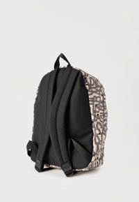 Πίσω όψη ενός σακιδίου με μαύρους μαξιλαρωτούς ιμάντες και μπεζ σώμα που διαθέτει αφηρημένο μαύρο γραμμικό σχέδιο σε λευκό φόντο.