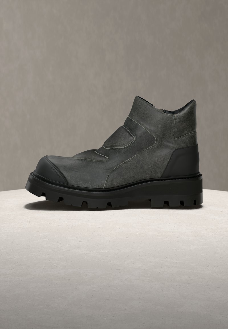 Dark gray leather ankle boot with thick black treaded sole and reinforced toe, displayed on a neutral surface with gray background.