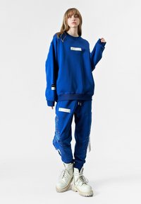 Sudadera oversized azul con un parche frontal y joggers azules a juego con detalles bordados. Combinado con botas blancas de tobillo.