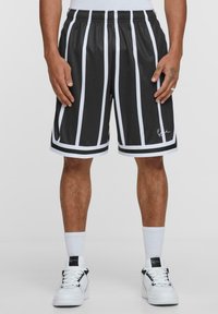 Svartvita randiga shorts med elastisk midja, slät yta och logotyp detalj vid fållen, bärs med vita sneakers och strumpor.