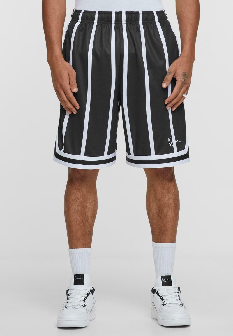 Svartvita randiga shorts med elastisk midja, slät yta och logotyp detalj vid fållen, bärs med vita sneakers och strumpor.