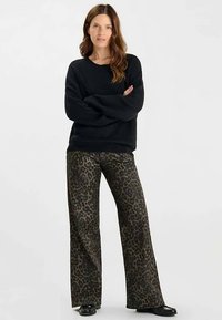 Zwart gestructureerd sweater gecombineerd met hooggetailleerde wijde broek met luipaardprint, met een ingetogen kleurenpalet en glanzende zwarte schoenen.