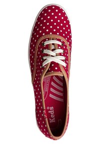 Baskets en toile rouge à pois blancs, accents beige et lacets blancs. Intérieur avec coussinage et logo de la marque. Forme à bout arrondi.
