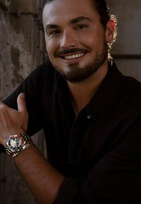 Silberne und rot-blau bezel Uhr mit einem schwarzen Zifferblatt, Stahlarmband, getragen am Handgelenk eines Mannes. Er trägt ein schwarzes Hemd mit Knöpfen.