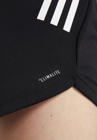 Svart sporttröja med fuktavledande textur, tre vita ränder på axeln och en "Climalite"-etikett nära fållen.