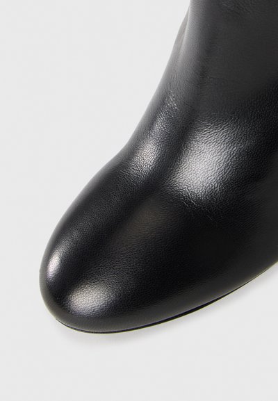 Close-up of smooth, shiny black leather boot toe with rounded shape against a plain light background.