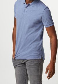 Polo tričko světle modré barvy, s krátkým rukávem, límečkem a zapínáním na dva knoflíky. Vyrobeno z texturované látky, stylizováno s bočními rozparky.