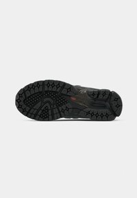 Semelle d'une chaussure de sport noire avec un motif de bande de roulement texturé pour une meilleure adhérence, comprenant des indentations hexagonales et en forme de losange ainsi qu'un logo rouge près du talon.