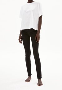Camiseta de algodón blanca de corte relajado, combinada con jeans negros ajustados. El conjunto presenta mangas cortas y un diseño simple.