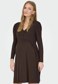 Bruine zwangerschapsjurk in een geribbelde textuur, met een V-hals, knoopdetails en lange mouwen, ontworpen voor comfort en stijl.