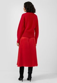 Czerwony sweter z dzianiny z okrągłym dekoltem i długimi rękawami, noszony na czerwonej spódnicy do kolan. Całość uzupełniają czarne kozaki za kolano.