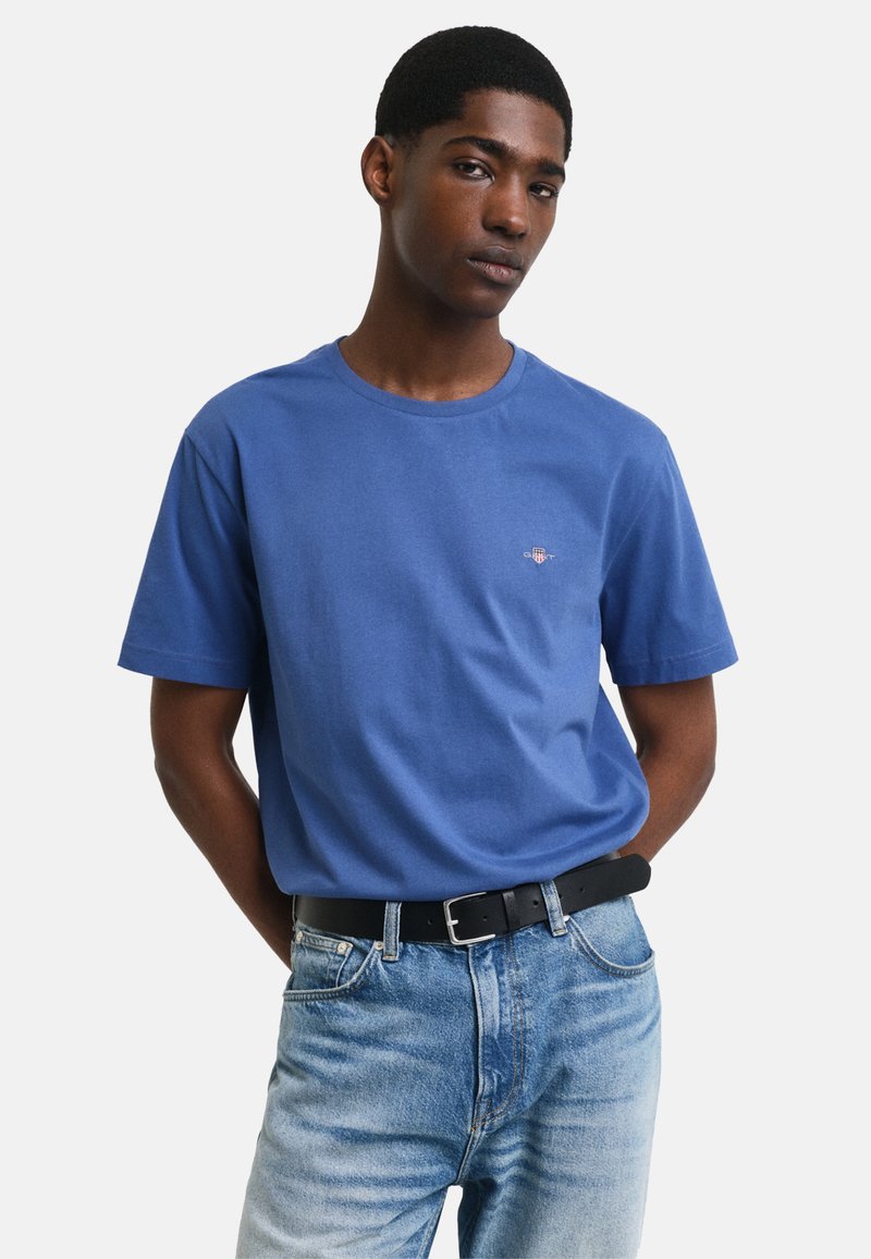 Blå bomullströja med rund halsringning och korta ärmar, med en liten broderad logotyp på bröstet, kombinerad med ljus tvättade denimjeans.