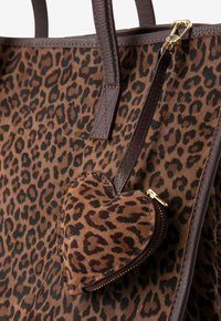 Sac fourre-tout en daim brun et noir à motif léopard avec des poignées en cuir brun ; comprend une pochette en forme de cœur détachable avec une fermeture éclair.