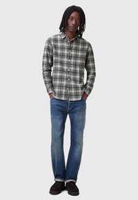 Geruite overhemd in zwart, wit en grijs met zakken. Blauwe denim jeans en zwarte schoenen maken de outfit compleet.