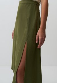 Jupe midi vert olive en tissu léger, dotée d'une fente haute sur un côté et d'une taille épurée avec un détail de fermeture discret.
