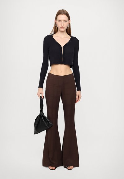 Black ribbed cropped cardigan with a front zipper, paired with high-waisted brown flared pants featuring a check pattern. Holds a black bag.