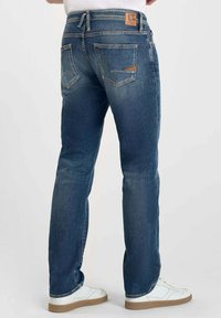 Jeans en denim bleu avec une coupe droite, dotés d'un patch en cuir sur la ceinture et de poches arrière avec des coutures contrastées.