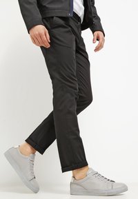 Svarta slim-fit byxor med en mjuk textur, kombinerat med ljusgrå lädersneakers med en minimalistisk design och snörning.