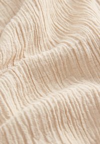 Tissu beige doux avec une texture froissée et chiffonnée créant des lignes horizontales fluides et inégales à travers la surface.