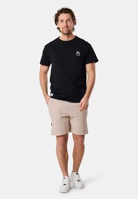 Un t-shirt en coton noir avec un petit logo sur la poitrine, associé à un short texturé beige clair et des baskets blanches.