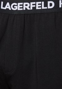 Shorts en coton noir avec une taille élastique portant l'inscription "LAGERFELD" en blanc. Texture lisse et éléments de design simples.