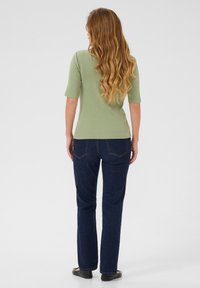 Haut côtelé vert à manches courtes, associé à un jean droit bleu foncé. Les cheveux du mannequin sont longs et ondulés, portés lâches.