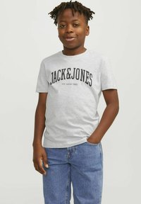 Camiseta gris de manga corta con "JACK&JONES" en texto negro en negrita; material de algodón de alta calidad. Se lleva con jeans de mezclilla azules.