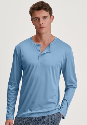 Lange mouwen, lichtblauw henley-shirt van zachte stof met een knoopsluiting. Model draagt een met patronen bedekte short voor contrast.